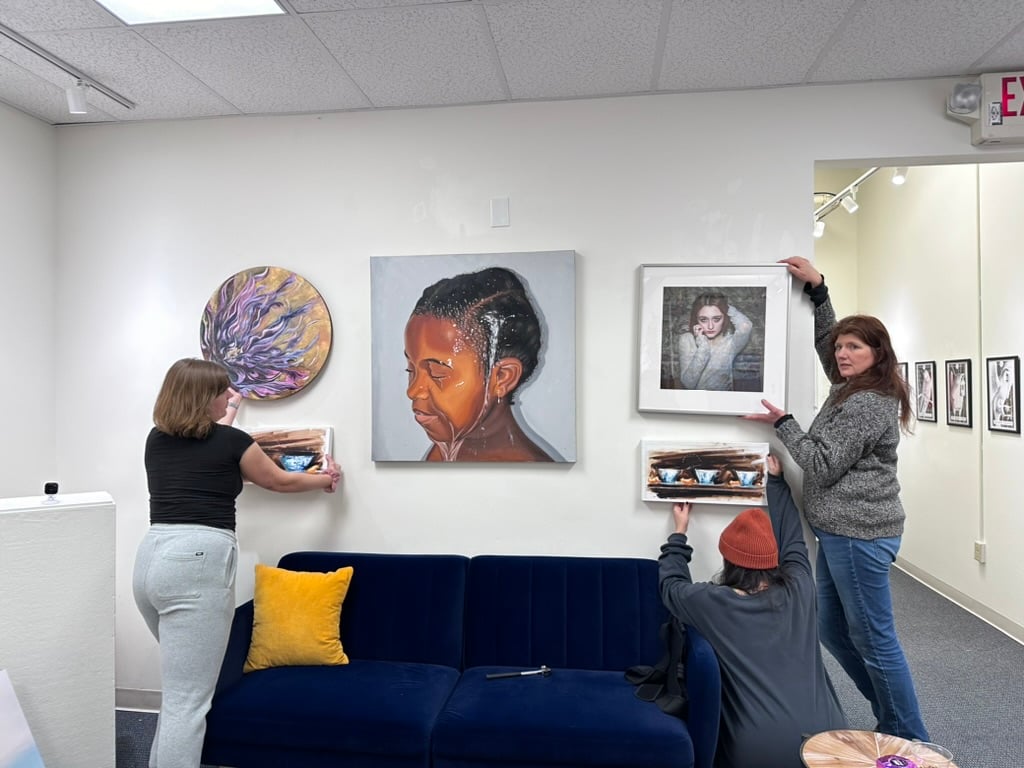 Three gallery staff members carefully hanging artwork on a wall