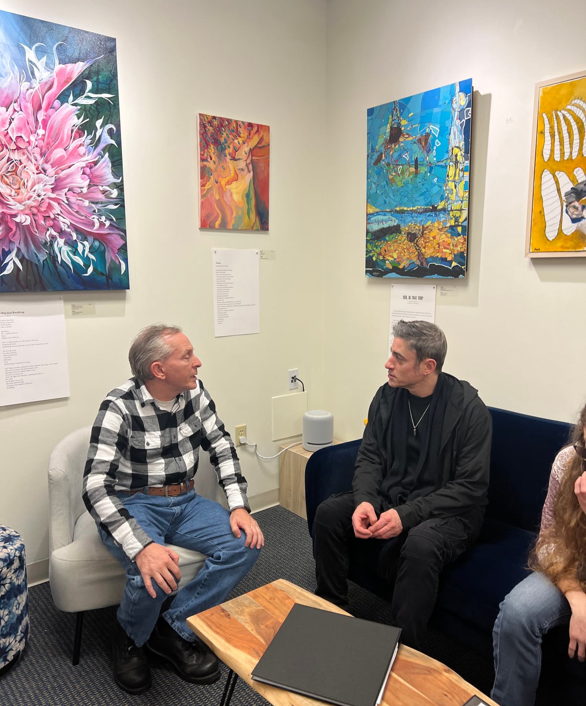 Two people in deep conversation in front of a wall of original paintings