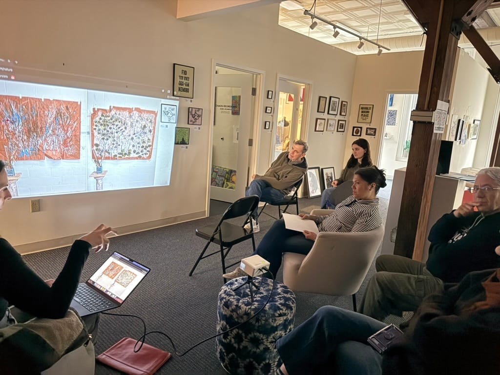 Group of jurors gathered around a presenter discussing work in a gallery