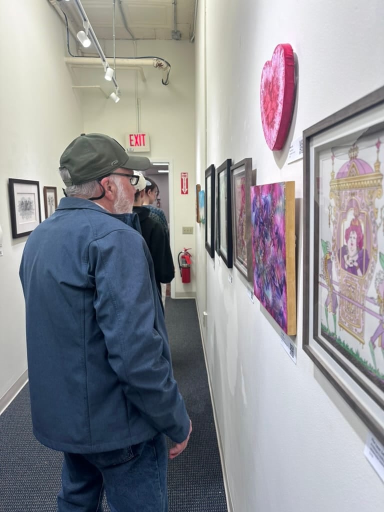 A juror studying a small framed work up close on a gallery wall