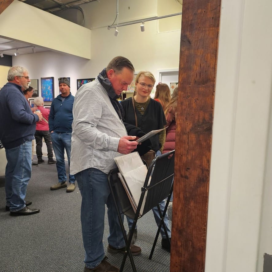Two gallerists in conversation in front of a wall of mixed-media paintings