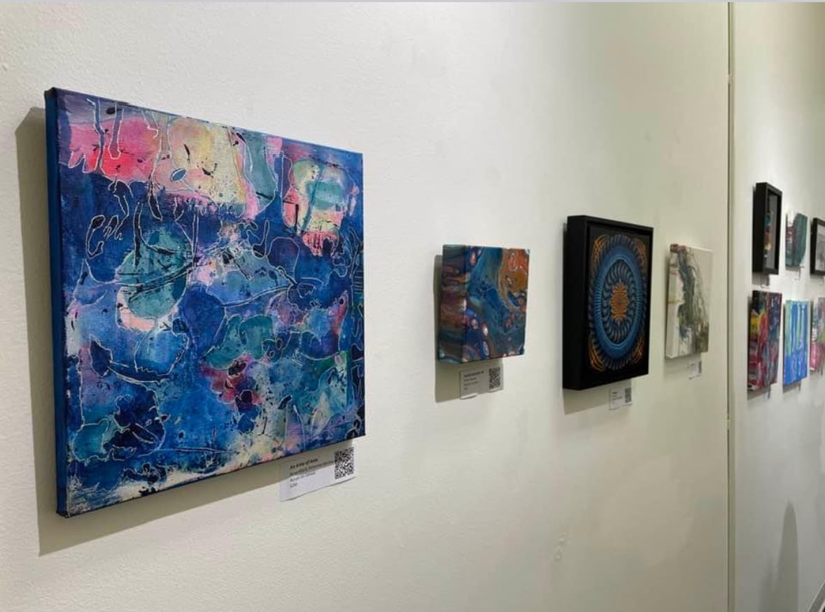 Original paintings on a gallery wall with QR-coded price tags below each piece